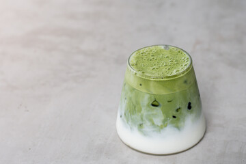 A glass of iced matcha green tea with milk on gray background. Antioxidant drink made of ground powder of green tea leaves.