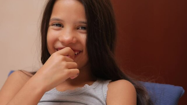 Young girl playfully biting nails while smiling and laughing
