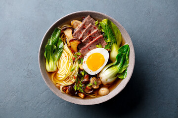 Asian noodle soup, ramen with beef, vegetables and egg in bowl. Grey background. Close up. Top view.