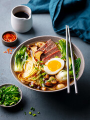 Asian noodle soup, ramen with beef, vegetables and egg in bowl. Grey background. Close up.