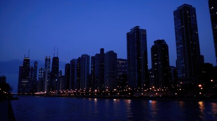 Obraz premium Night skyline of a city with illuminated buildings and reflections on water.