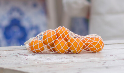 Still life of tangerines in a mesh bag on a white wooden table