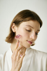 Vertical shot of Caucasian woman using rose pink face roller to massage face