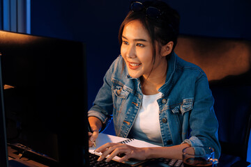 Smiling young beautiful asian creative officer looking on pc in sales target online, earning job's...