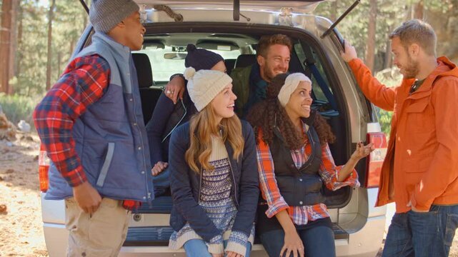 Group of young friends outdoors sitting in open tailgate of car before walk through autumn or fall countryside - shot in slow motion