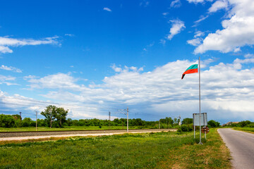 Fototapeta premium Railway tracks and the Bulgarian national flag under cloudy May sky at the exit of the village of Krum in direction of the town of Dimitrovgrad in Haskovo Province, Southern Bulgaria