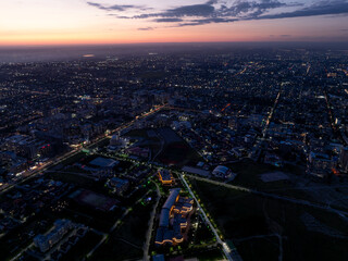 Obraz premium City landscape. Evening view from a drone of the city at sunset. Trees, roads, streets, cars and buildings. Beautiful summer scenery.