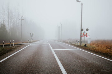 A misty railroad crossing with metal tracks and a deserted road, surrounded by fog and rural grassland. The muted colors evoke a serene, atmospheric scene.