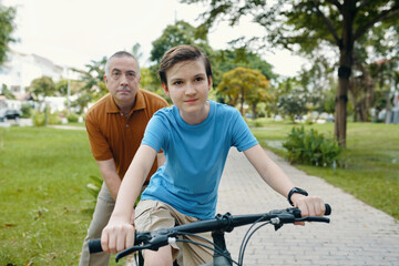 Obraz premium Child riding a bike in the park with his grandfather helping him