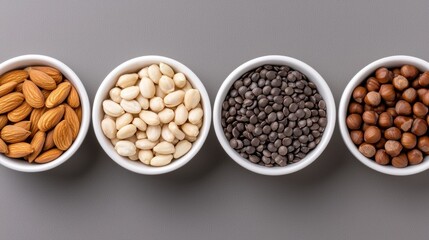 Four white bowls of different types of nuts arranged in a row on a gray background.