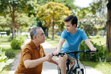 Obraz premium Grandfather spending time with his grandson in the park while they riding a bike