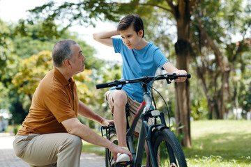 Fototapeta premium Grandfather showing his grandchild how to control the bike while they spending time in the park