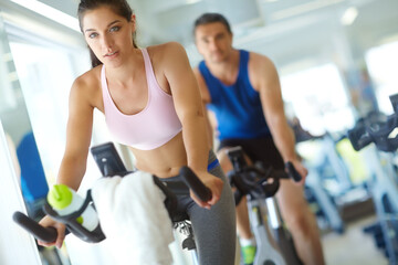 Fototapeta premium Gym, couple and woman with bicycle for training, intense workout and collaboration for cardio health. Session, man and partner with machine for cycling, fitness and exercise for wellness with balance