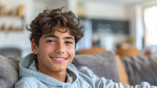 A young man with curly brown hair and a gray hoodie is smiling at the camera.