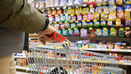 Close-up of a customer's hand holding a shopping trolley in the sweets and candies section
