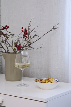 Imagine a serene setup with white wine, snacks of cheeps with dry branches and red berries, and stylish decor for a relaxing.