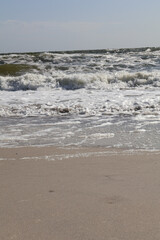 A vibrant seascape showcasing ocean waves crashing onto the sandy shore with white foam under a clear sky