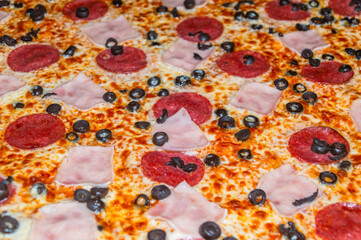 Close-up of pizza with ham, salami and black olives.
