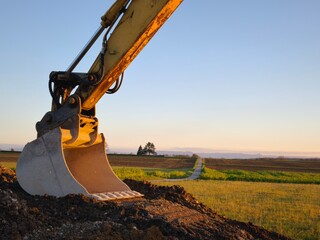 An excavator bucket rests on a mound of earth. The view stretches to the horizon
