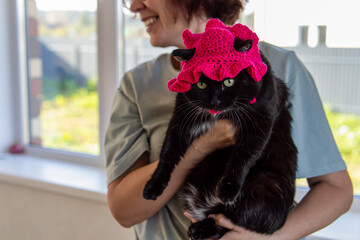 Woman holds a black cat in a pink knitted panama hat. Natural. Crocheted beanie