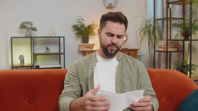 Stressed brunette man in living room looking at unpaid bank debt bills, doing paperwork, planning budget, calculate finances mortgage payments, deadline. Male guy throws paper bills at home apartment.
