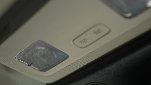Driver pressing button to turn on and off lamp lights at the car ceiling trim headliner, close up.