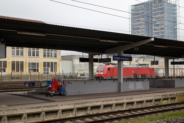 Naklejka premium A red passenger train arriving at a railway station platform on a cloudy day. The train is partially covered by a station canopy.