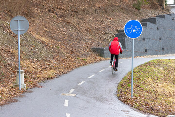 A man in a red jacket rides a bicycle along a marked bicycle path, during a dry spring day.