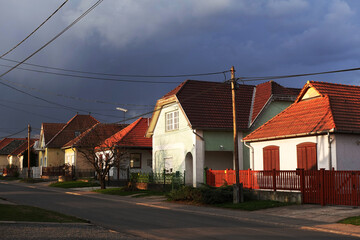 Obraz premium Quiet street in a rural village with colorful houses and red roofs under a dramatic stormy sky.