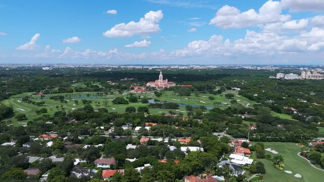 Aerial view of Biltmore Hotel in Coral Gables, Miami. Expansive green landscape of golf course surrounding historic hotel with clear blue sky and scattering clouds above