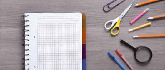 Notebook with graph paper and various colorful school supplies arranged on a gray wooden table, creating a learning or studying concept. Back to school banner