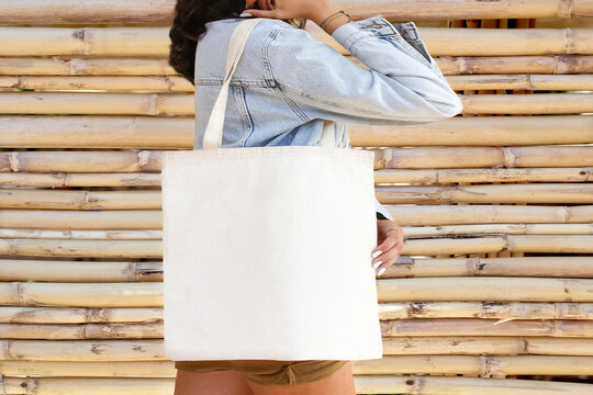 Woman is holding bag canvas fabric for mockup blank template. white cotton bag for your design. Young woman with cotton bag on street, closeup.  Mockup for design