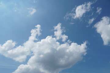 Obraz premium White fluffy clouds in the sky. Blue sky and cloud cover on a sunny summer day. Empty background, copy space