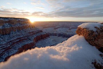 A breathtaking sunrise casts warm light over the snowy Grand Canyon, highlighting its majestic layers and creating a serene winter wonderland.