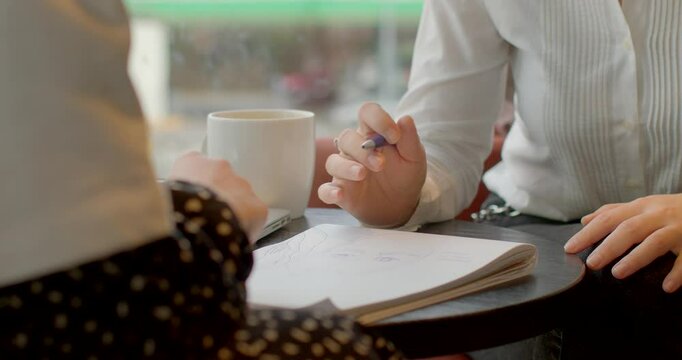A closeup view of hands actively engaged in a meeting, with notes scattered and coffee cups on the table