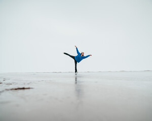 Caucasian woman in a blue sweater is skating on a frozen lake. Figure skater performs a swallow. 