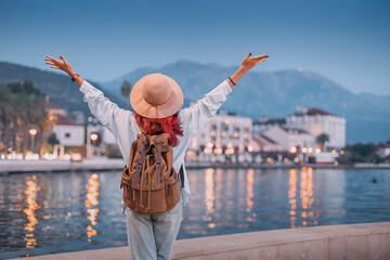 Carefree tourist with backpack enjoying freedom in front of beautiful cityscape by the sea at sunset