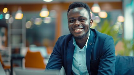 Obraz premium A portrait of a smiling Black man in a blue blazer and light blue shirt seated in a modern office. The background is blurred
