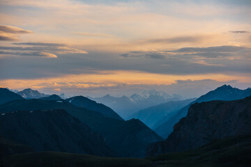 Deep gorge between layered silhouettes of sharp rocky ridge spurs under huge snowy mountain peak in...