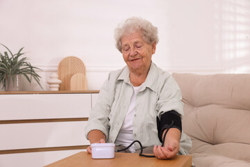Senior woman measuring blood pressure at wooden table indoors