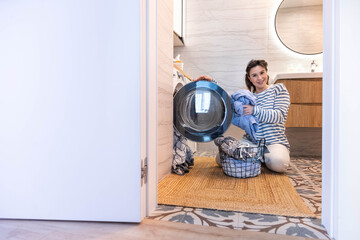 Smiling woman housewife cleaning linen textile clothes putting washing machine and dryer at laundry