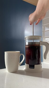 Pressing freshly brewed coffee in a French press, paired with a clean white mug on a bright countertop. The rich aroma of coffee fills the air in a minimalist, sunlit kitchen