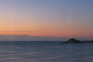 Naklejka premium 夕焼け・夕方・朝焼け・日の出の太陽に照らされた海と砂浜の波の風景 グラデーションのかかった空と低い雲 オレンジと紫の美しい空と色に染まった海面と太平洋の水平線 バカンス・旅行・観光・アウトドア・チルのイメージ