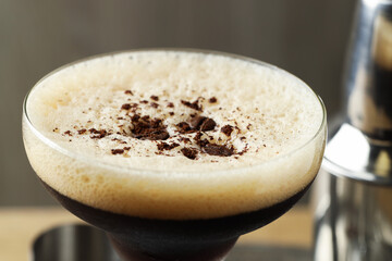Delicious espresso martini with coffee beans in glass on blurred background, closeup