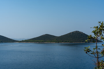 View of two green hills surrounded by the blue sea on sunny day. Ideal for inspiration when travelling and exploring the coast. High quality photo