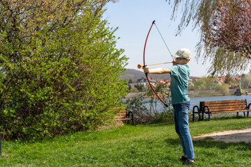 Boy practicing archery with toy bow and arrow in park by the river on sunny day. Concept of outdoor...