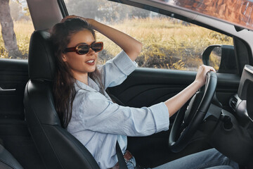 Naklejka premium A woman in sunglasses sits in the driver's seat, her hand on the steering wheel, and her head tilted to the side, capturing a relaxed and confident driving moment