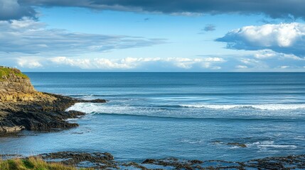 Obraz premium Tranquil Coastal View Featuring Rocky Shoreline, Calm Blue Waters, and Dramatic Cloudy Sky Over Serene Ocean Landscape in Scenic Nature Setting
