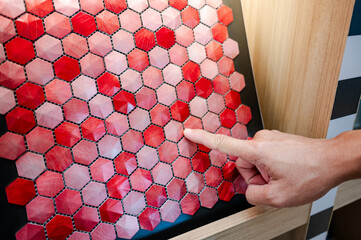 Designer hand pointing at red hexagon pattern mosaic tile on ceramic collection display shelf in...