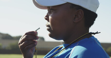 Side view close up of a middle aged biracial female rugby coach standing on a sports field blowing a